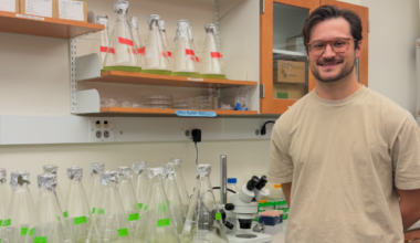 Evan Stair in a laboratory beside several flasks containing green liquid