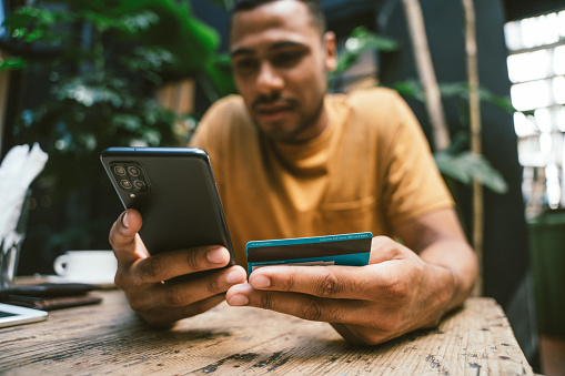 Man making online payment using smartphone and credit card in coffee shop