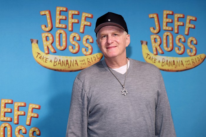 Michael Rapaport stood wearing a grey jumper and black baseball cap, smiling ahead.