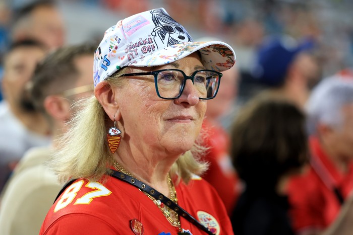 Donna Kelce wearing a football shirt and baseball cap, standing sidewards to the camera.