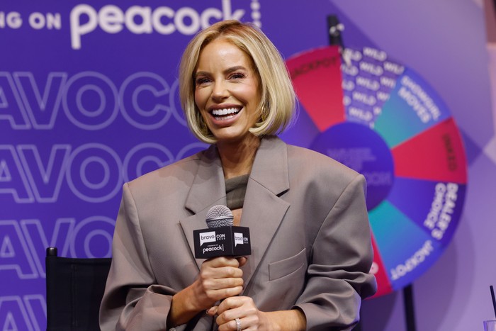 Caroline Stanbury holding a microphone with both hands and smiling ahead.