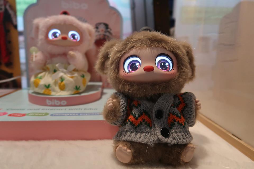 A Labubu-like AI toy with brown fur and big eyes and wearing a gray sweater 