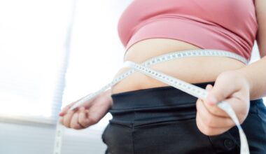 Overweight woman in pink sports top pulling measuring tape around waist