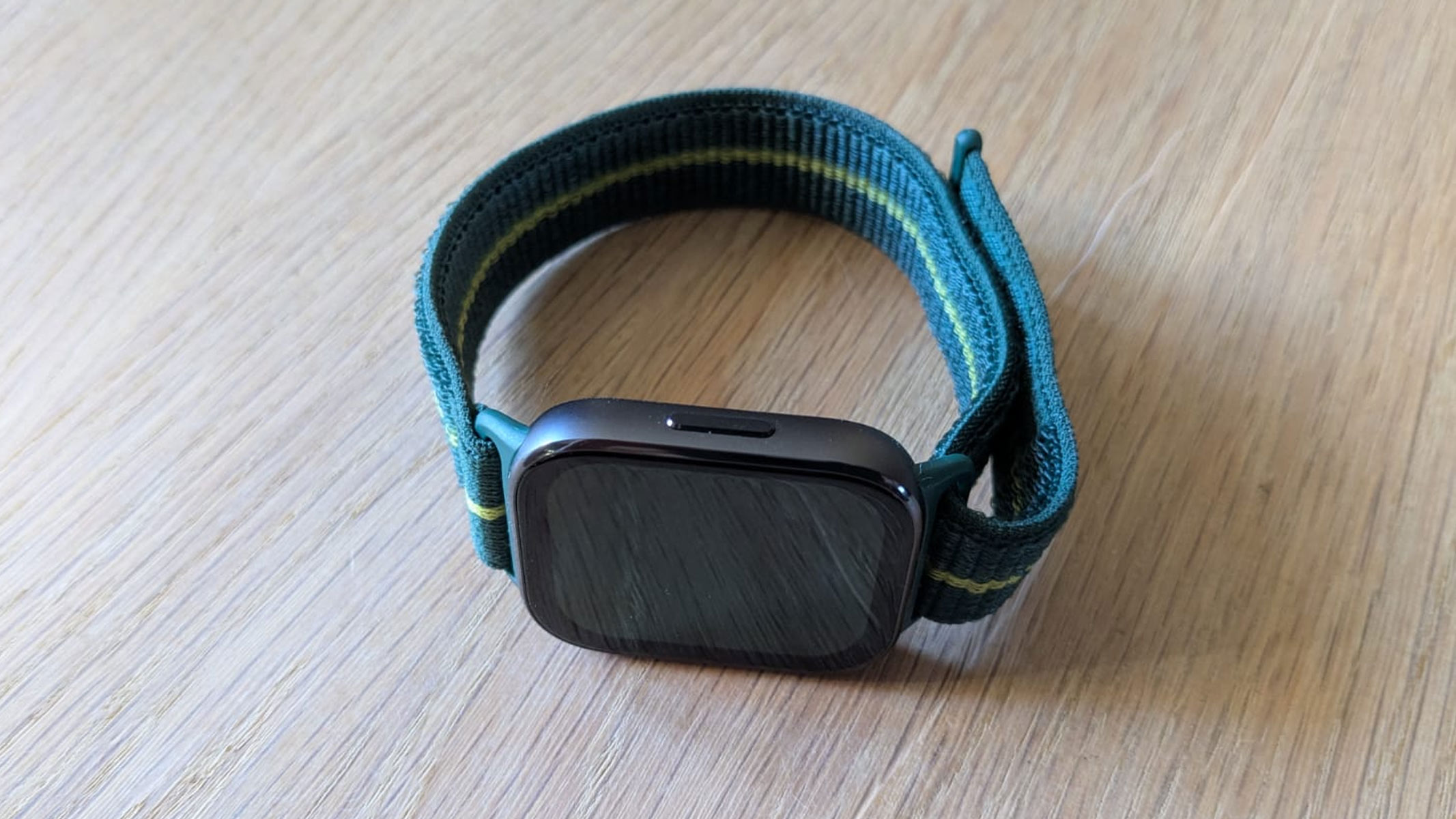 The Motorola Moto Watch Fit on a wooden table, picture taken from a bird's eye view to show the side button.