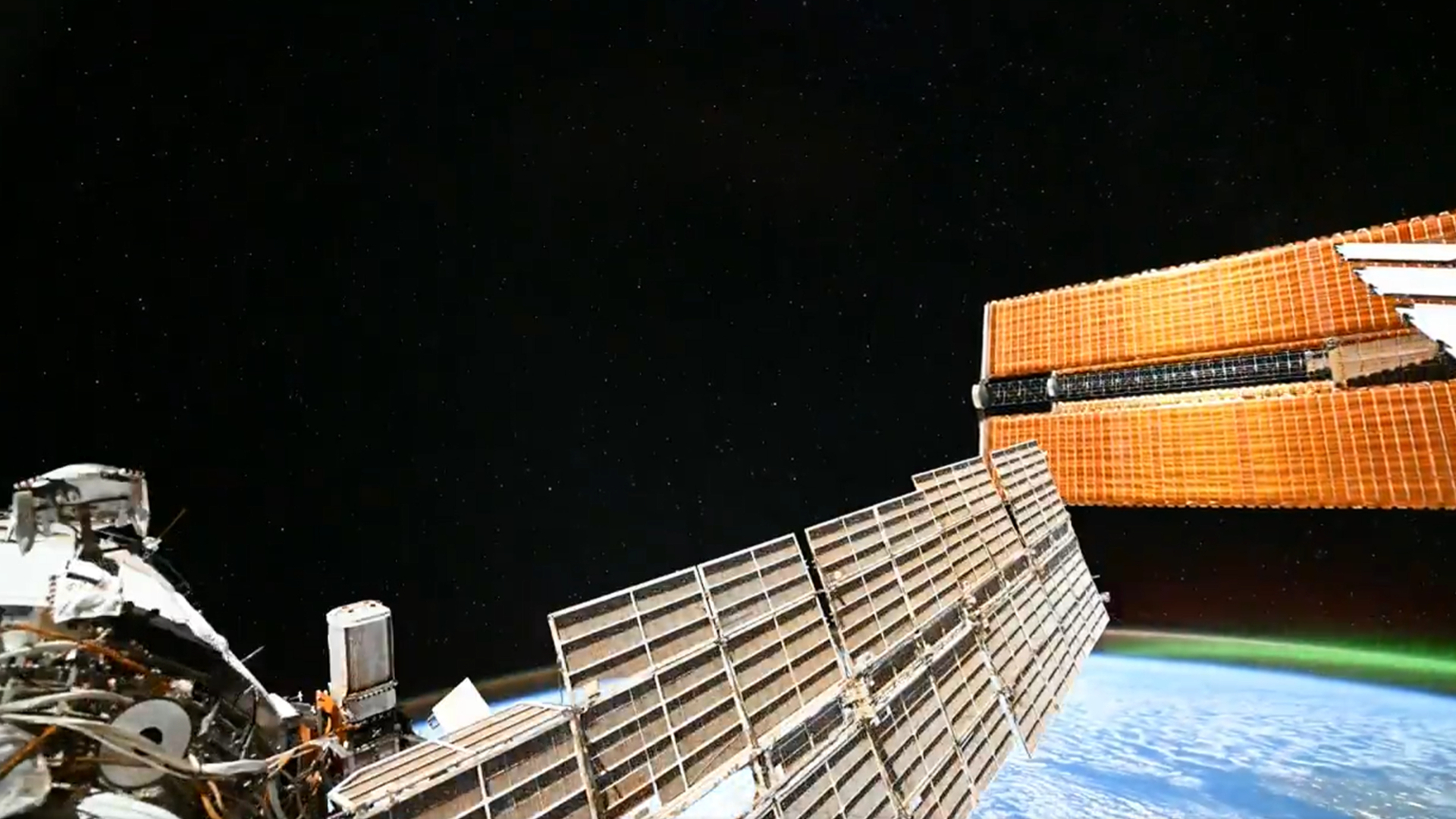 An image of low Earth orbit captured from the International Space Station, showing the curve of Earth at the bottom of the screen with the black of space beyond. The outer hull of the station is visible at the bottom of the screen, as are solar panels.