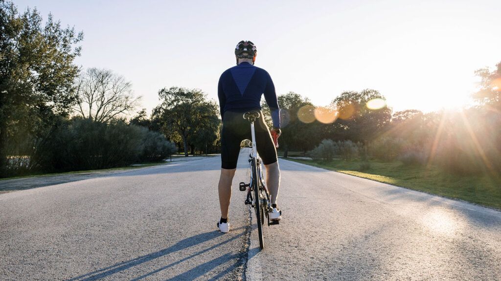 A man riding a bicycle in cycling gear on a road at sunset.