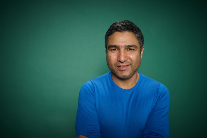 RT_CoverParty_Celeb_Traitors-187 Nick Mohammed at the Radio Times Covers Party, stood in front of a green backdrop and wearing a blue top.