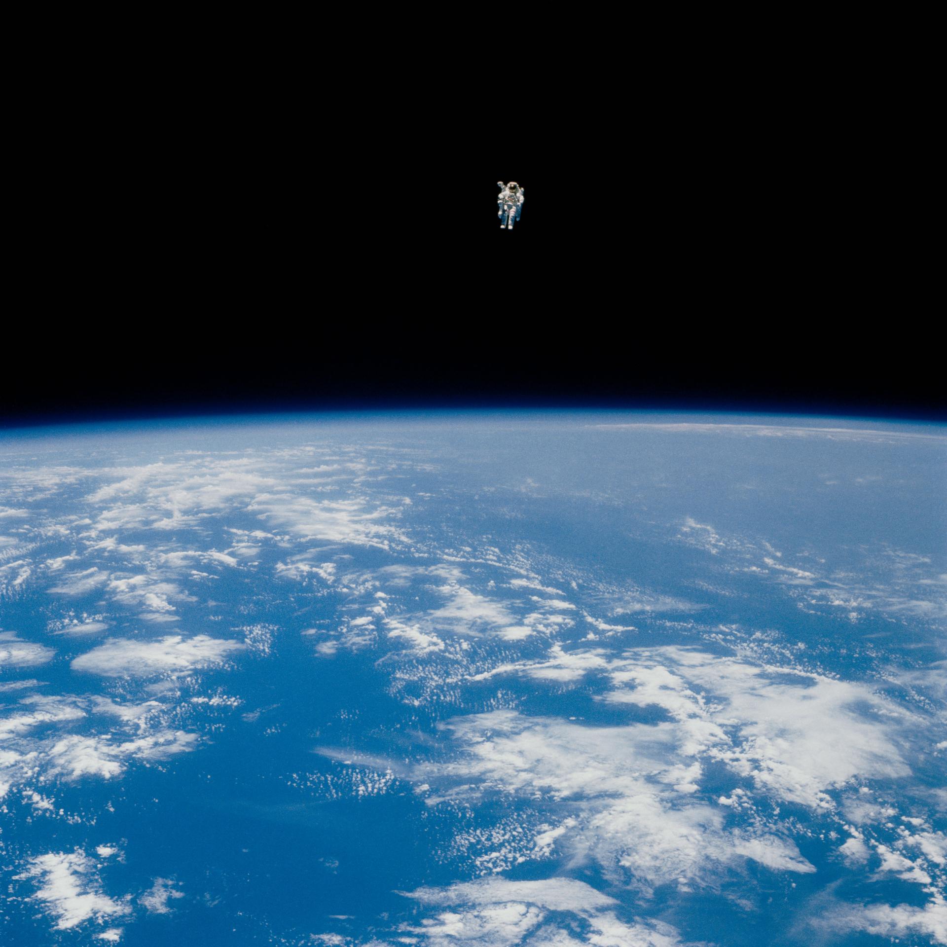 An astronaut in a spacesuit floats alone above Earth, with the planet's blue surface and clouds visible below against the blackness of space—an image capturing humanity’s quest for discovery.