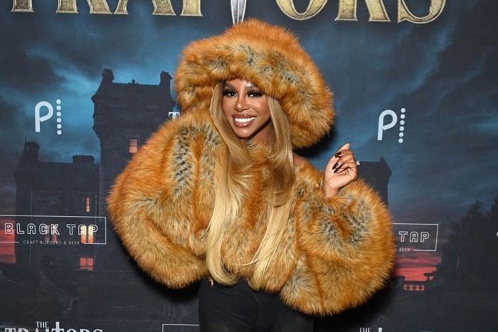 Candiace Dillard Bassett smiling ahead wearing a brown faux fur jacket and matching oversized faux fur hat.