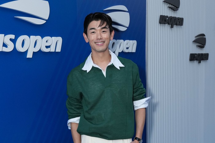 Eric Nam wearing a green jumper, stood and smiling ahead with one hand in his pocket.