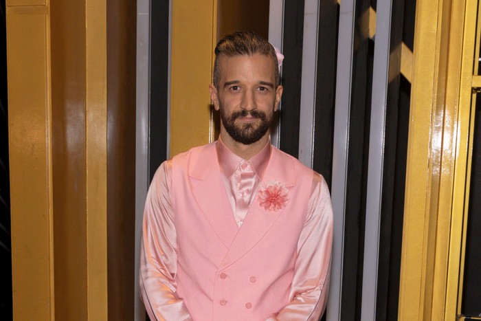 Mark Ballas wearing a matching pink suit and shirt, stood with his hands clasped in front of him and smiling ahead.