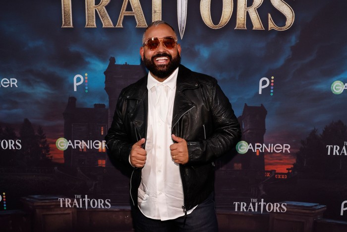 Yamil "Yam Yam" Arocho smiling ahead, wearing sunglasses and holding the lapels of his jacket.