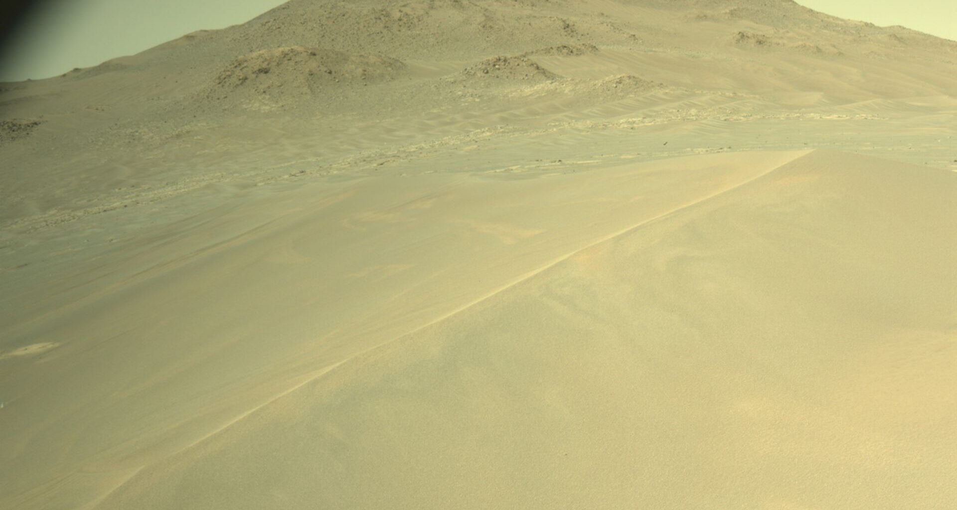 A greenish tinted image with a large hill in the distance and smaller sandy dunes in front