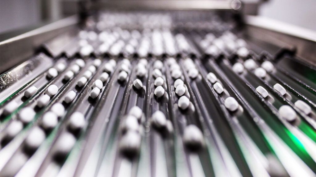 Rows of weight loss pills are on a conveyer belt in a pharmaceutical lab