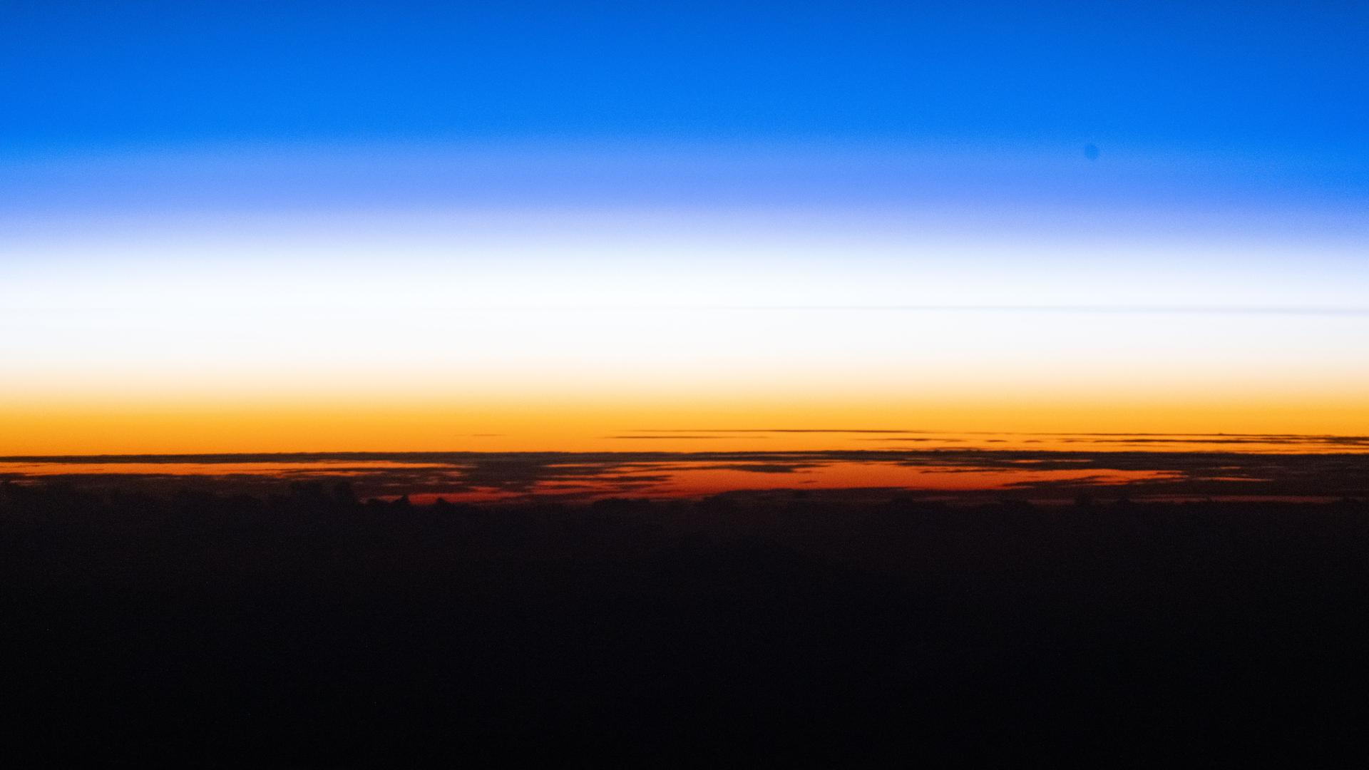 A sunset showing the black curve of the Earth with a golden band of light just above and a blue band of light above that