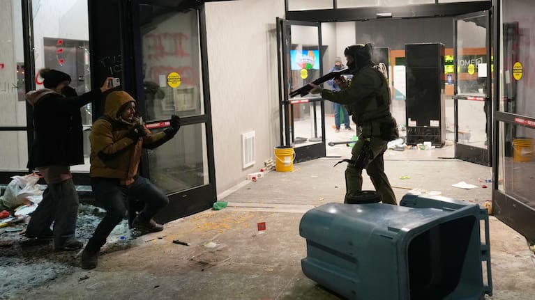A federal agent points a weapon at a person outside a hotel during a noise demonstration protest in response to federal immigration enforcement operations in Minneapolis.