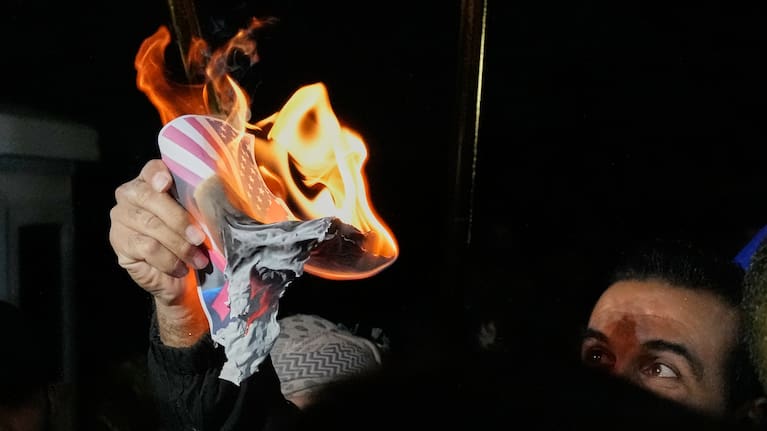 A protester holds an image of a U.S. flag and President Donald Trump set on fire during a protest against the threats by Trump that the U.S. would no longer support the country.