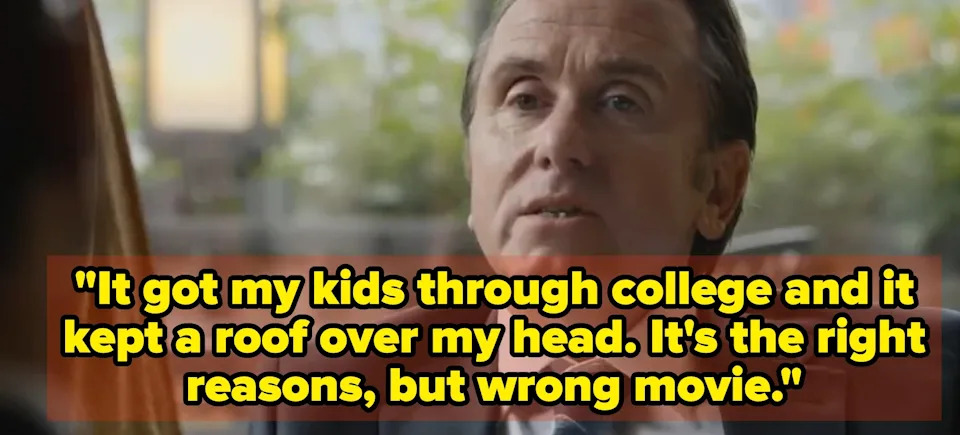 A person in a suit and tie is seated indoors, engaging with another person who is partially visible in the foreground