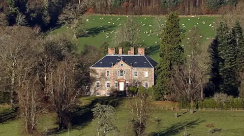 Walter Baxter Torwoodlee House in the Borders - an impressive brick building with a number of chimneys nestled between trees with farmland around