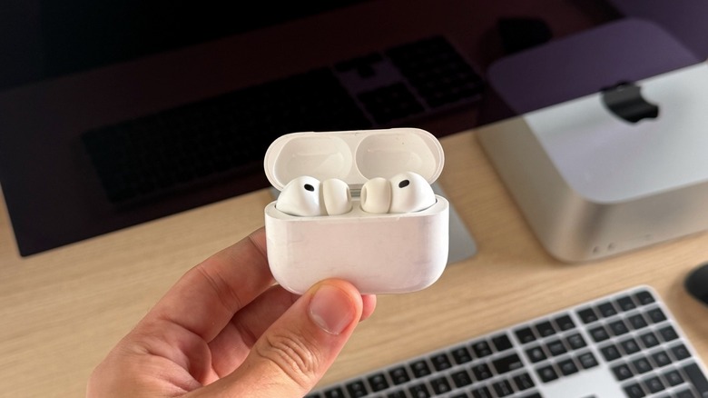 AirPods Pro 3 inside the charging case with the Mac Studio and Studio Display behind it