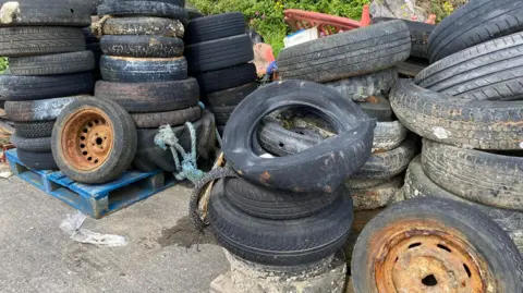 The Ships Project A pile of tyres which have been retrieved from the seabed in Plymouth Sound. Some are stacked up on blue pallets.