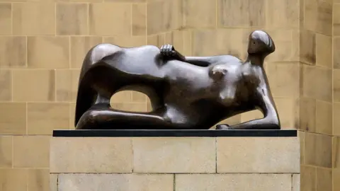 Leeds City Council A bronze statue on a plinth. The figure is reclining in a relaxed manner. The wall behind is light stone.