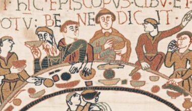 a section of the bayeux tapestry depicting six men around a crescent table eating and drinking. a man below serves wine.