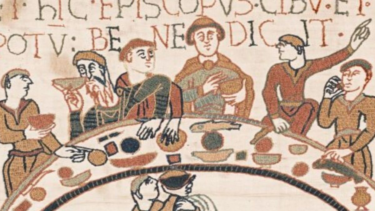 a section of the bayeux tapestry depicting six men around a crescent table eating and drinking. a man below serves wine.