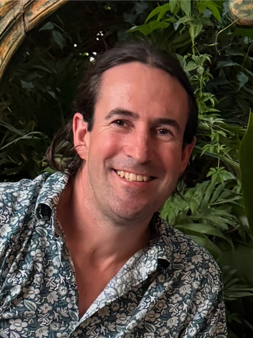 A smiling, dark-haired man in a floral shirt.