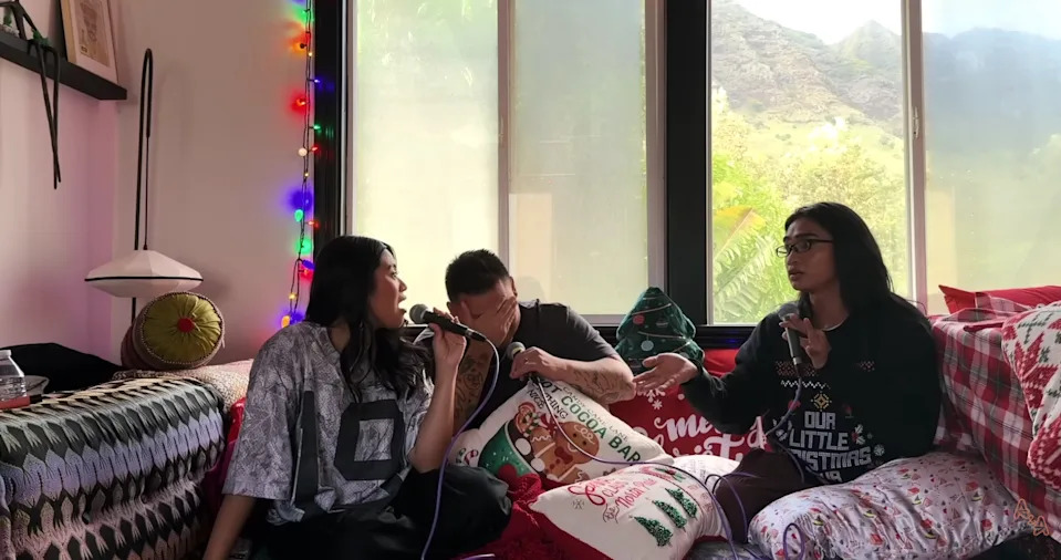 Bretman Rock and the Sweet and Savory podcast hosts sit on a couch with festive pillows, engaging in conversation inside a cozy, decorated room