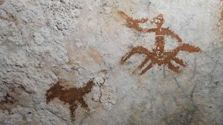 Cave drawings in Sulawesi, Indonesia of a human figure and a bird with a faded handprint in between them.