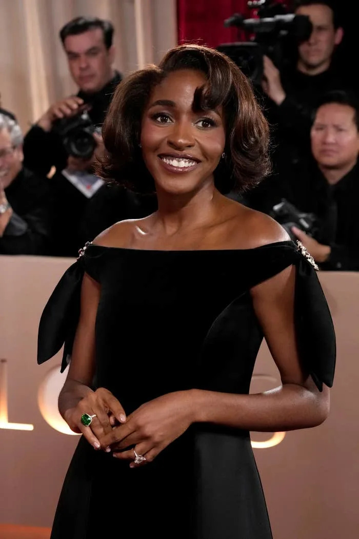 Ayo Edebiri on a red carpet, smiling, surrounded by photographers