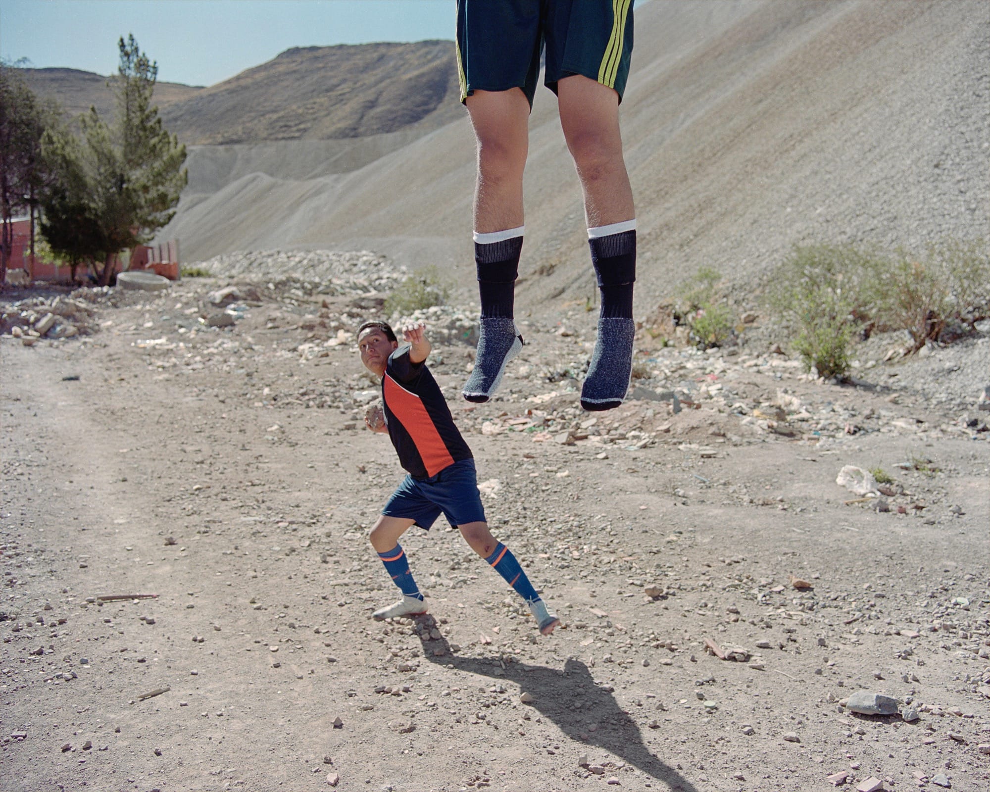 A photograph by River Claure of two people playing soccer, with one jumping high enough their their top half is out of the frame and only their legs are visible