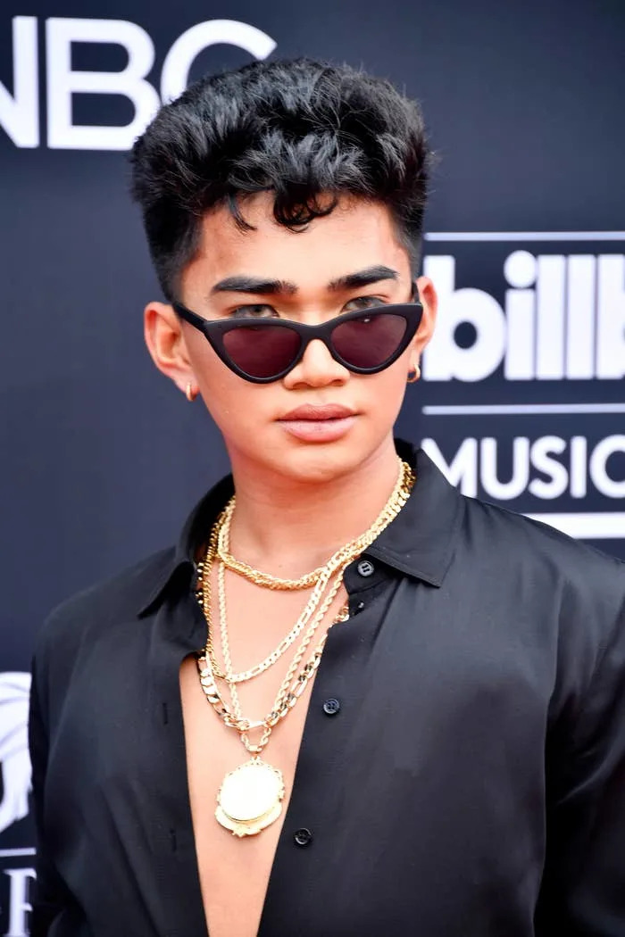 Bretman Rock in sunglasses and multiple gold chains attends a formal event, wearing a shirt with an open collar