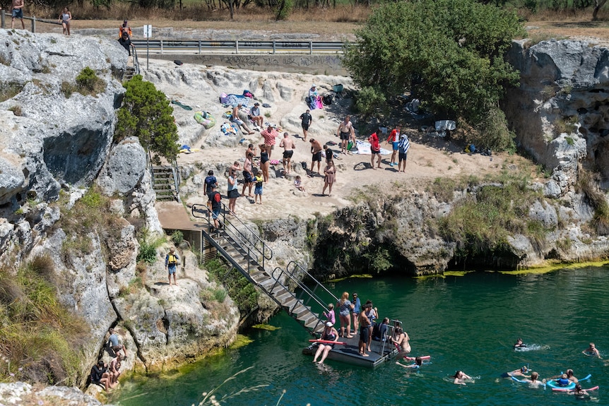 Stairs leading down from cliffs into a lake of water, with swimmers in the water and at the top of the stairs