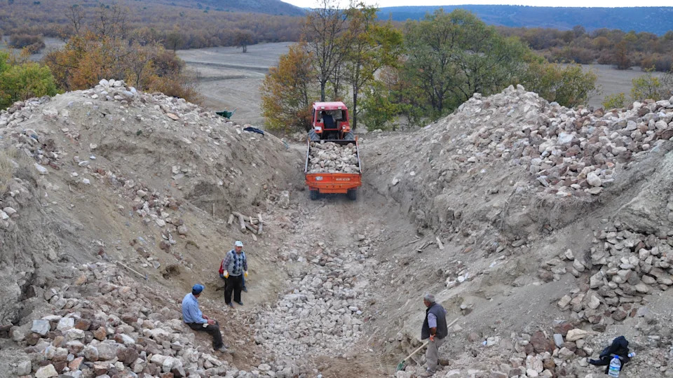 archaeologists stand in a rocky trench with a bulldozer
