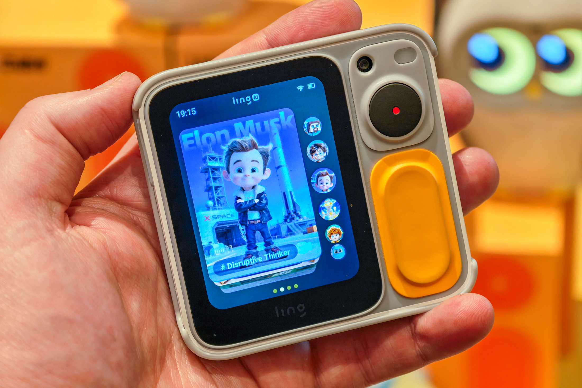 A palm-sized device with a small screen displaying a cartoon version of Elon Musk.