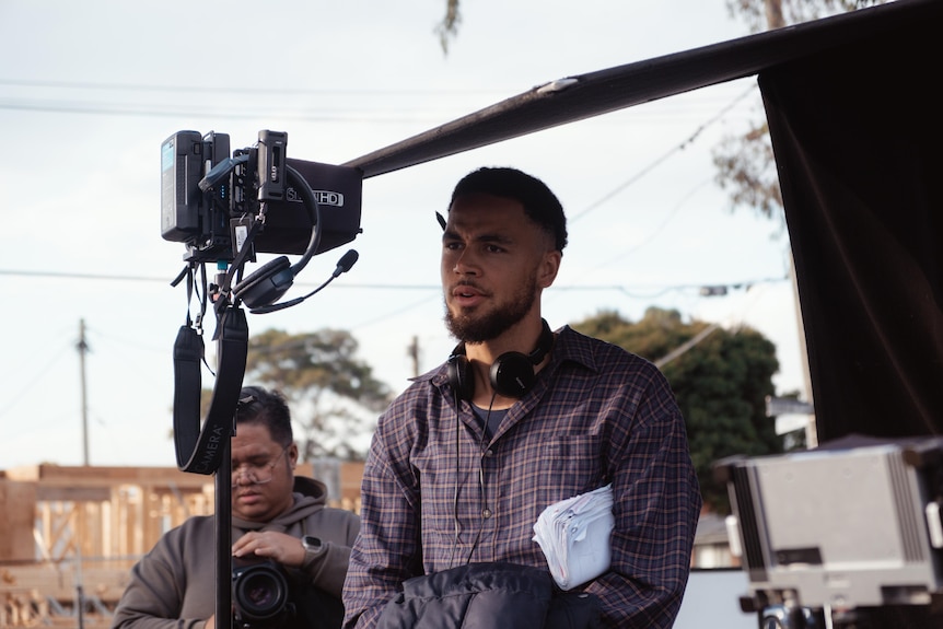 Kalu Oji with a pen behind his ear and headphones around his neck standing next to recording equipment.