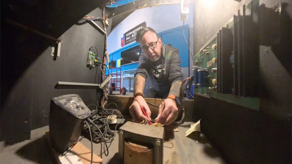 An engineer kneels down behind an arcade machine with a multimeter in his hand. He's helping to check that Space Invaders is in full working order.
