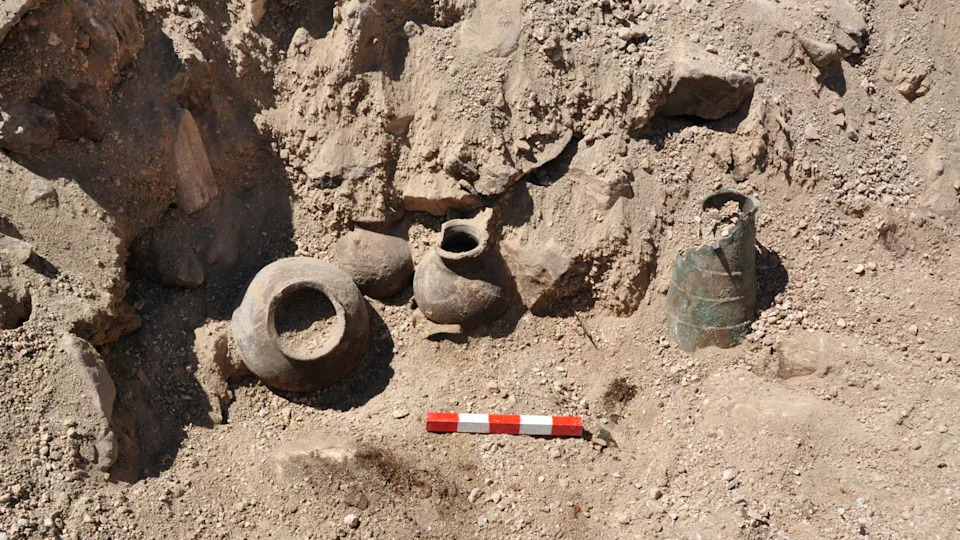 several ceramic jars and a bronze pot being excavated on an archaeological site