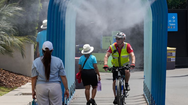 Fans walk and ride bikes through a water mister at the Australian Open tennis championship in Melbourne.