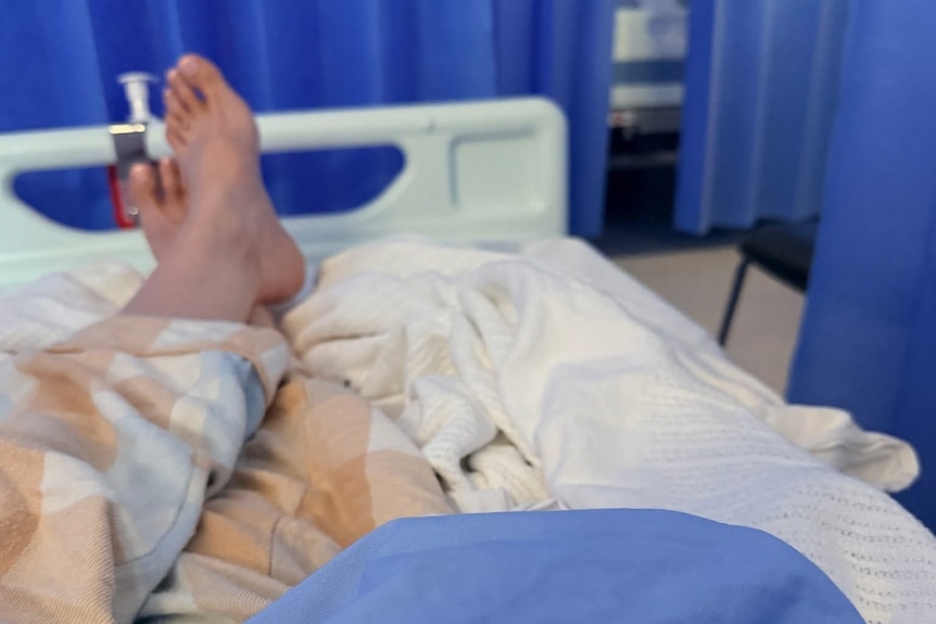 Legs and feet on hospital bed, surrounded by blue curtain.