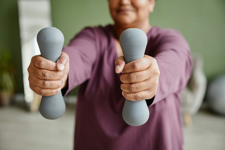 a woman holding a pair of small dumbells