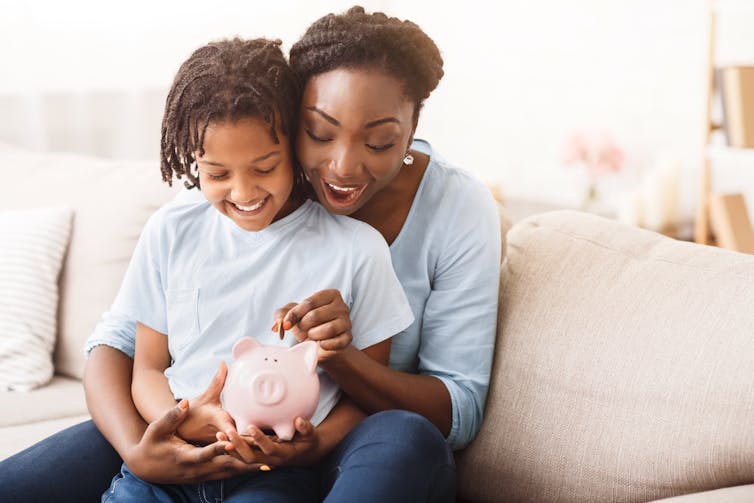 mother and young child slotting a coin into a piggy bank and smiling.