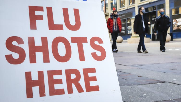 A large sign reading 'Flu shots here' in the foreground with a street scene in the background