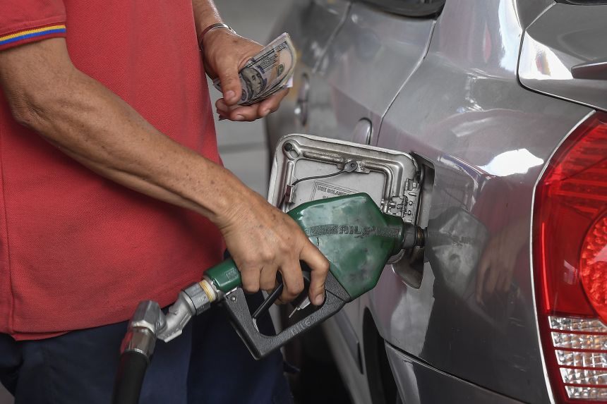 A worker holds a gas pump and US dollars at a Petroleos de Venezuela SA (PDVSA) gas station in Caracas, Venezuela, on December 1, 2022.