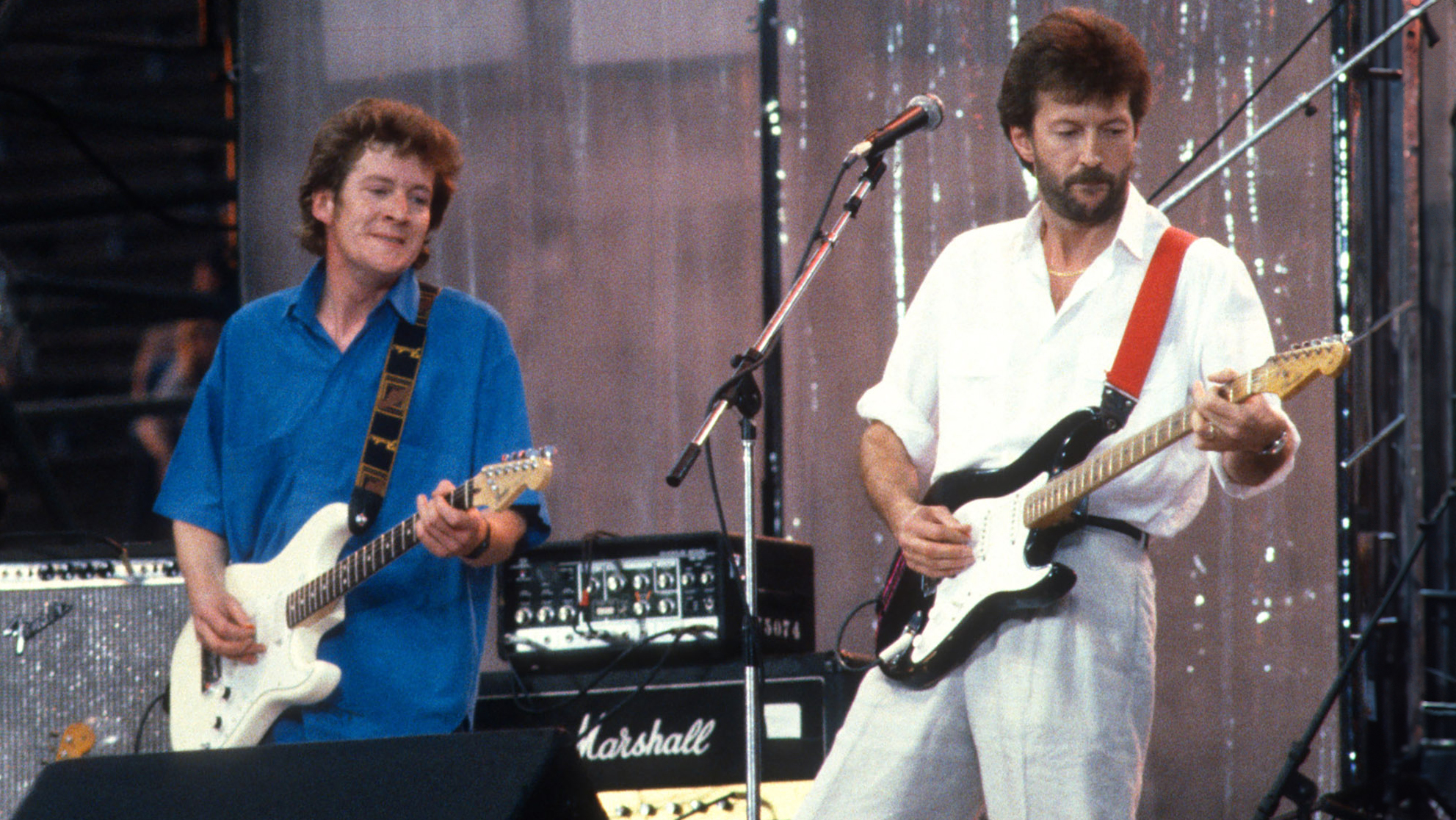 English Rock &amp; Blues musician Eric Clapton (right) performs, with his band, during the Live Aid benefit concert, onstage at JFK Stadium, Philadelphia, Pennsylvania, July 13, 1985. Also visible are Shaun Murphy (left), on tambourine, and Tim Renwick (center), on electric guitar.