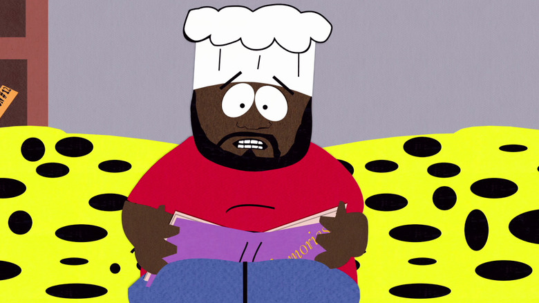 Chef reads from a book while wearing his chef's hat and red shirt on a bright yellow couch in "South Park"