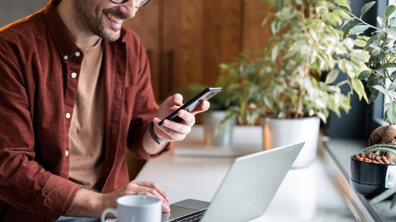 Man using phone while using laptop