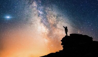 Lone person standing on top of rock, pointing towards the vivid cloudy Milky Way and the vast expanse of universe.